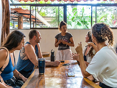 Sprachschüler sitzen im offenen Gemeinschaftsraum der Expanish Sámara Schule und sprechen mit ihrer Lehrkraft.