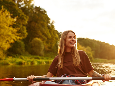 Junge Frau beim Kajakfahren auf einem ruhigen Fluss bei Sonnenuntergang in der Natur