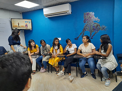 Gruppe von jungen Erwachsenen sitzt in einem modernen Klassenraum in Neu-Delhi und nimmt aktiv an einer Englisch Sprachlektion teil.