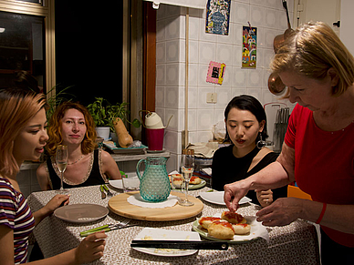 Internationale Sprachschüler sitzen gemeinsam mit ihrer Gastfamilie am Esstisch in der Küche beim gemeinsames Abendessen.