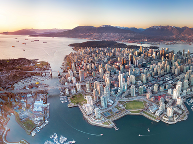 Luftaufnahme von Vancouver mit dicht bebauter Skyline, Hafen und umliegenden Bergen bei Sonnenuntergang