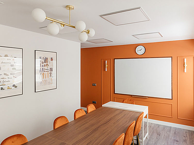 Modernes Unterrichtszimmer der Expanish Sprachschule mit orangefarbenen Akzenten und großem Whiteboard.