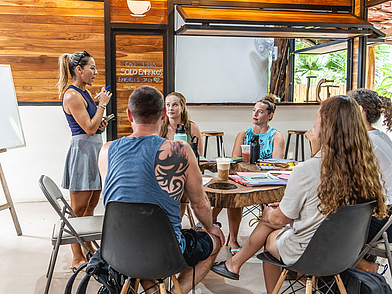 Dozentin führt lebhaften Spanischunterricht in einer kleinen Gruppe Erwachsener im tropischen Ambiente der Expanish Sámara Schule.