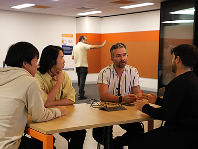 Eine kleine Gruppe internationaler Sprachschüler sitzt mit einem Lehrer an einem Tisch in der ILSC Adelaide und diskutiert im Englischunterricht in einer modernen Lernumgebung.