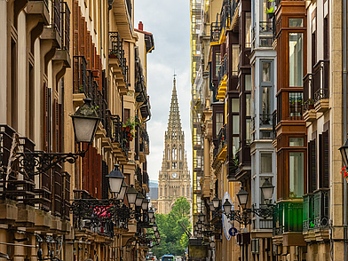 Blick durch eine enge Gasse in der Altstadt von San Sebastián auf die eindrucksvolle Kathedrale Buen Pastor – ideal, um während der Sprachreise Kultur und Geschichte zu entdecken.