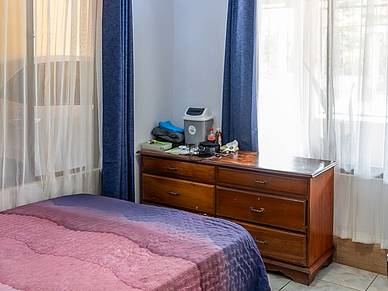 Schlafzimmer mit Holzkkommode, bunner Bettdecke und großen Fenstern in einer Gastfamilie der Expanish Sprachschule Sámara.