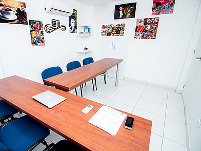 Heller Unterrichtsraum in der Sprachschule ECOS Cartagena mit langen Holztischen und kulturellen Postern, optimal für interaktive Sprachübungen.